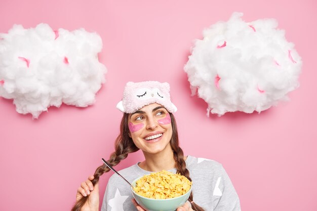 Dreamy lovely woman holds pigtail thinks about something pleasant while eating breakfast