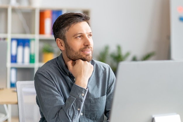 Dreamy mature businessman thinking of new business strategy sitting at workplace in office looking