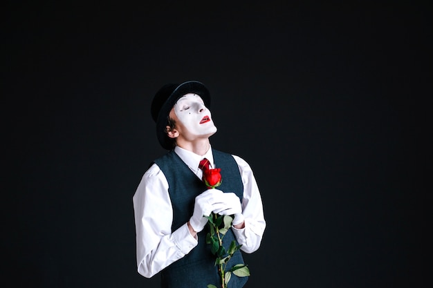 Dreamy mime stands with red rose on black background