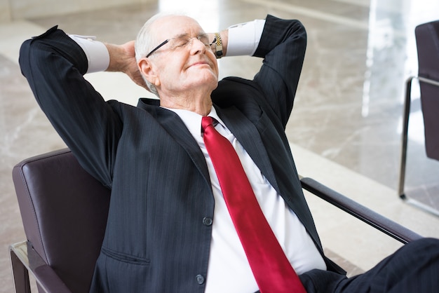 dreamy senior Caucasian businessman wearing glasses resting in armchair