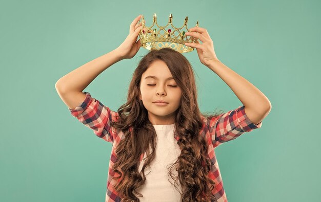 Dreamy teen girl with curly hair wear crown on blue background smug