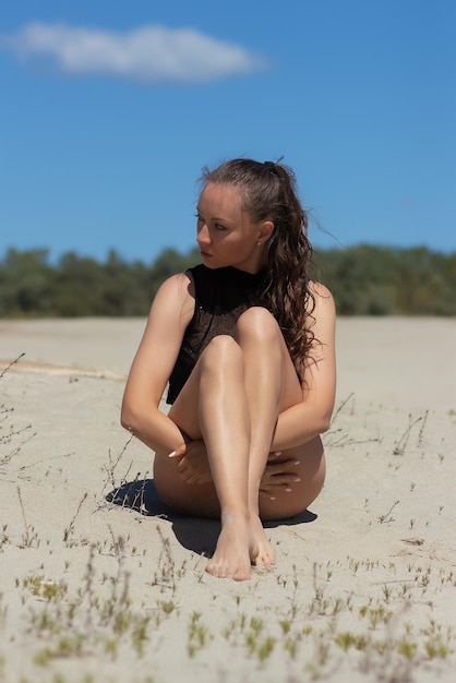 Dreamy woman in beachwear sitting on sandy beach