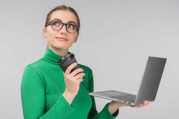 Dreamy woman holds a cup of coffee and laptop in her hands