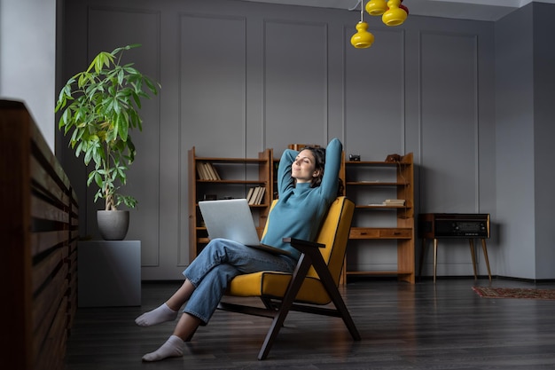 Dreamy woman rest after finished work look in window sitting stretching hands behind head relaxing