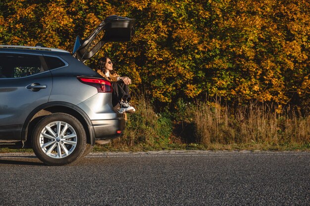 A dreamy woman sits in the trunk of her car and enjoys the autumn sunset