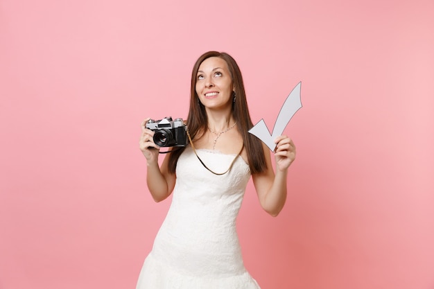 Dreamy woman in white dress looking up hold retro vintage photo camera and check mark, choosing staff photographer 