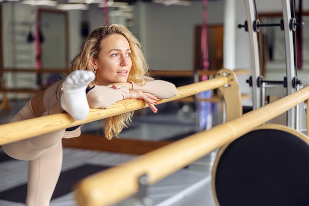 ジムでピラティスマシンで運動しながら目をそらしている夢のような若いフィットの女性スポーツ用品アクティブで健康的なライフスタイルのリハビリの概念