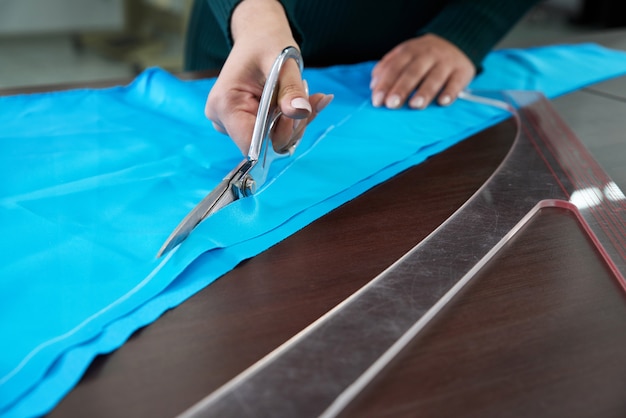 Dressmaker cutting blue fabric in tailor studio