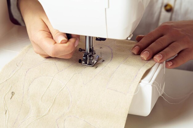 Dressmaker hand using sewing machine putting white soft fabric with stitch contour on needle plate under presser foot