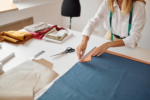 Dressmaker measures cloth at her workplace in workshop. Dressmaking occupation and professional sewing, handmade tailoring business, handicraft hobby