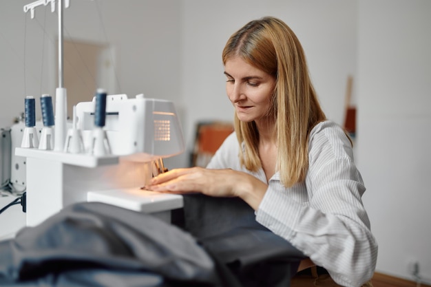 Dressmaker sews cloth on sewing machine at her workplace in workshop. dressmaking occupation, handmade tailoring business.