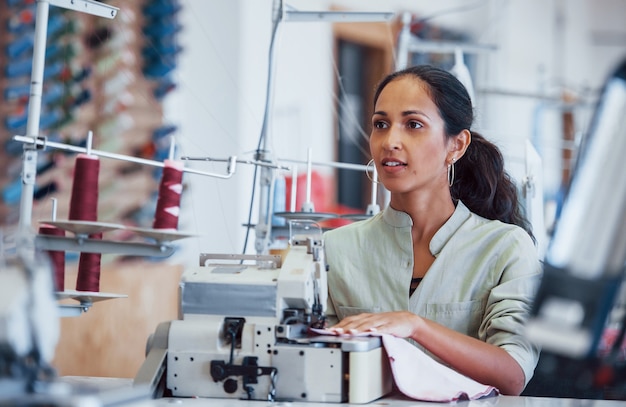 Dressmaker woman sews clothes on sewing machine in factory.