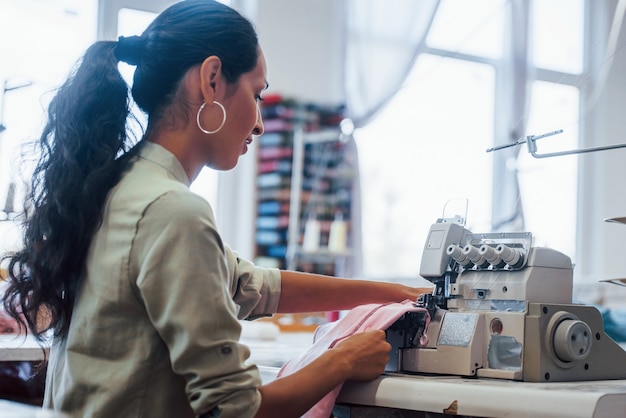 Dressmaker woman sews clothes on sewing machine in factory.