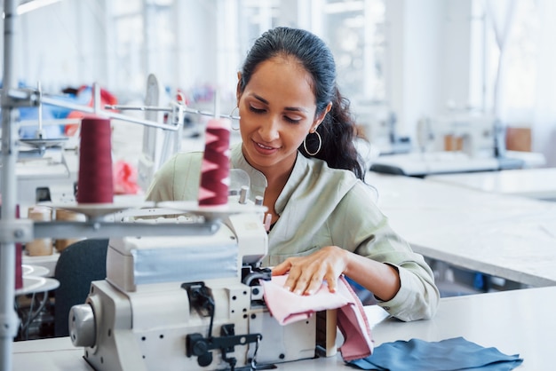 Dressmaker woman sews clothes on sewing machine in factory.