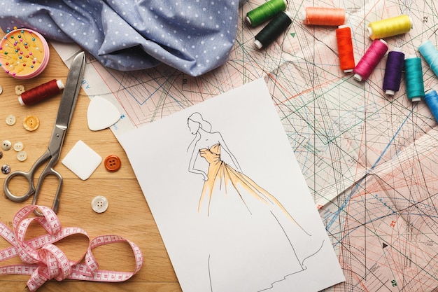 Dressmaking and fashion collection background. Drawn sketches, sewing patterns and various designer accessories on messy table, top view. Creativity concept