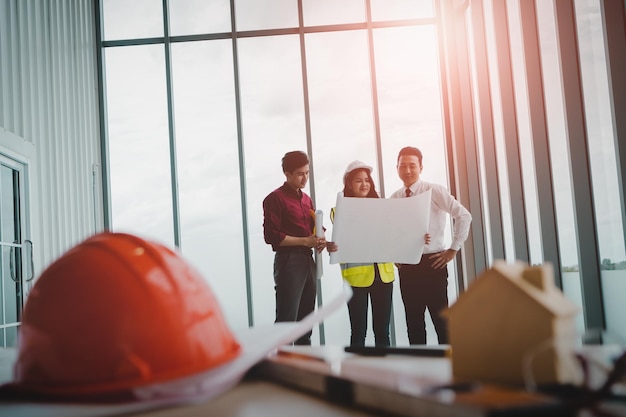 Drie aannemersteam is aan het brainstormen over een bouwplan aan het uiteinde van het bureau voor thuisontwikkelaars met constructiehulpmiddelen met lichte flare van de windowsxa