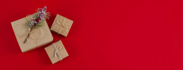 Foto drie ambachtelijke geschenkdozen met jute draad en vuren tak op een rode achtergrond