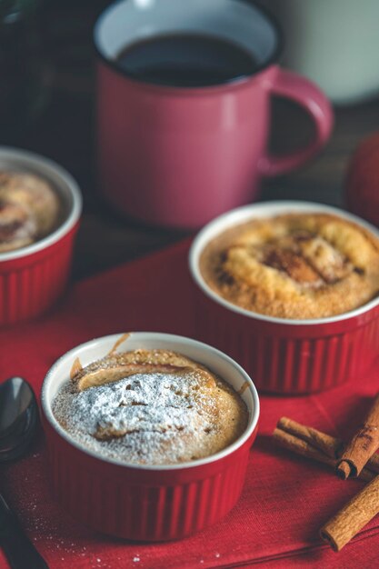 Drie appeltaartjes in keramische bakvormen met rode servet ramekin op een donkere houten tafel.