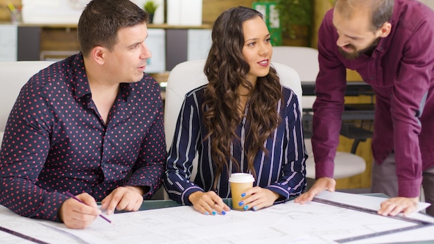 Drie architecten en ontwerpers praten over blauwdrukken die op tafel liggen