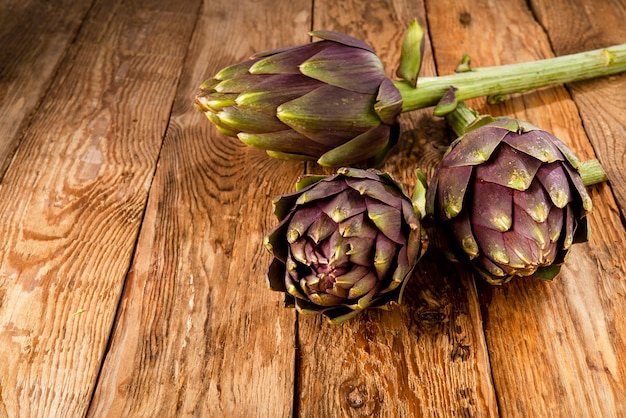 Drie artisjokken op een oude houten plank rustieke plantaardige sfeer