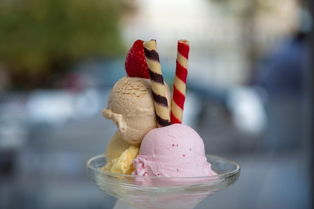 Drie bolletjes ijs van verschillende smaken en kleuren in een glas met ongerichte achtergrond