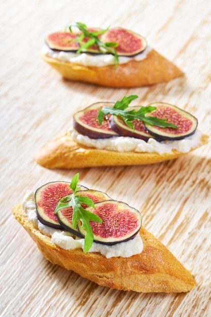 Drie bruschetta met ricotta en verse vijgen op een witte houten tafel, verticale compositie.