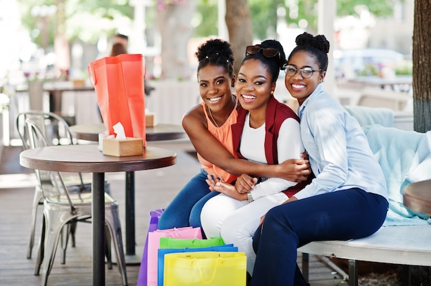 Drie casual afro-amerikaanse meisjes met gekleurde boodschappentassen buiten lopen. stijlvolle zwarte dames winkelen.