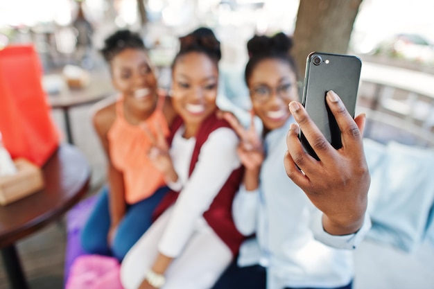 Drie casual Afro-Amerikaanse meisjes met gekleurde boodschappentassen die buiten lopen Stijlvolle zwarte dames winkelen en selfie maken op de telefoon