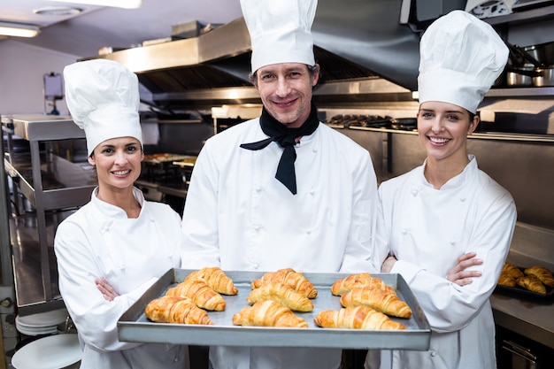 Drie chef-koks die een dienblad met gebakken croissant houden