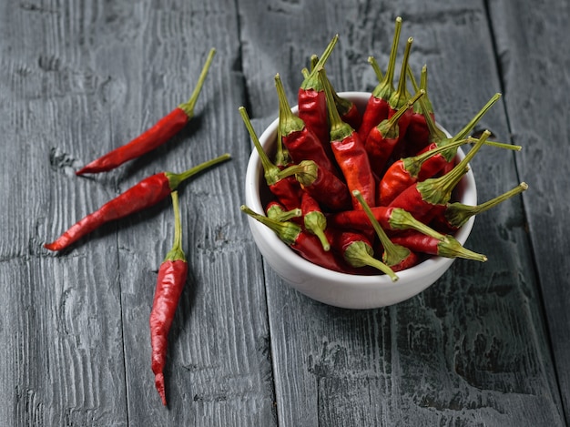 Drie chili pepers en een witte kom van paprika's op een donkere houten tafel