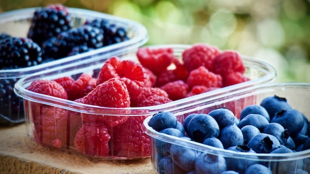 Drie containers met frambozen, bosbessen en bosbessen liggen op een tafel.