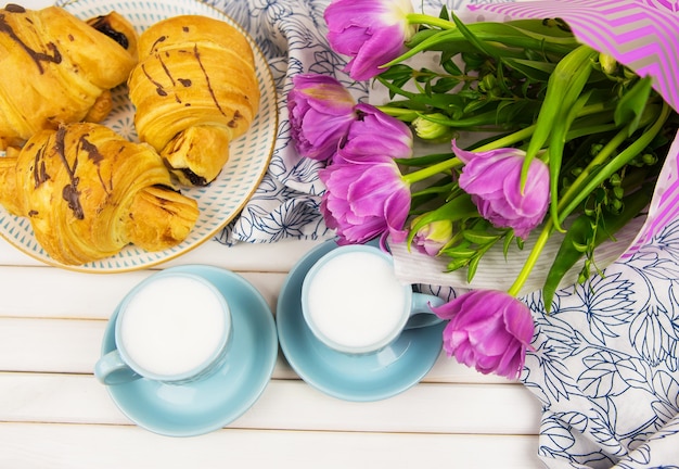 Foto drie croissants, twee kopjes koffie op tafel en een boeket prachtige tulpen-close-up