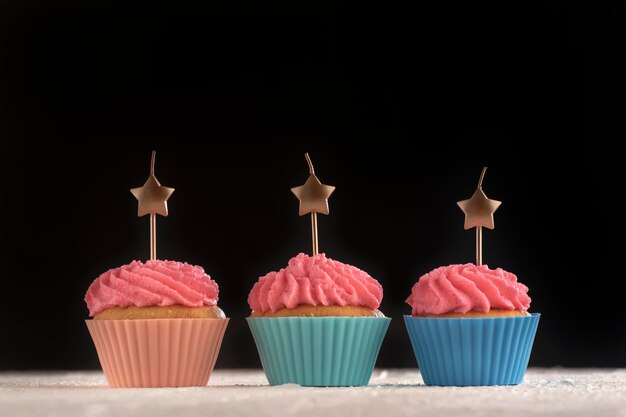 Drie cupcakes met roze buttercream frosting met kaarsen in de vorm van een ster op zwarte achtergrond. ruimte kopiëren.