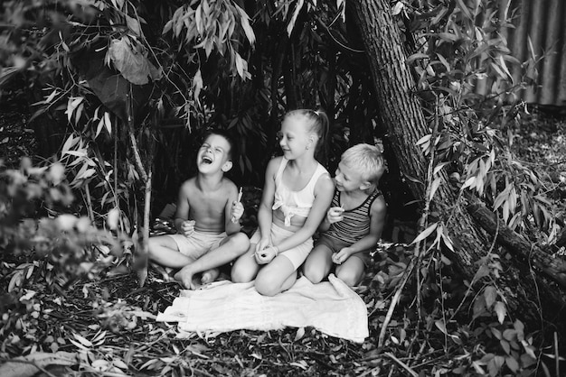 Drie dorpskinderen spelen in een hut die ze zelf hebben gebouwd van bladeren en takjes Houten huis in het bos Zwart-wit fotografie