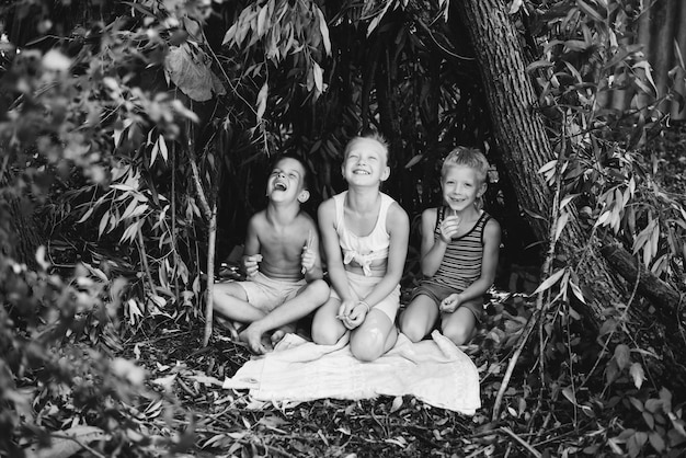 Drie dorpskinderen spelen in een hut die ze zelf hebben gebouwd van bladeren en takjes Houten huis in het bos Zwart-wit fotografie