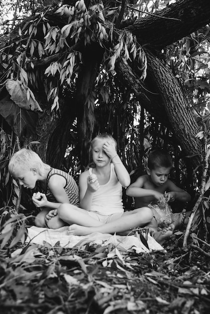 Drie dorpskinderen spelen in een hut die ze zelf hebben gebouwd van bladeren en takjes Houten huis in het bos Zwart-wit fotografie