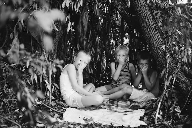 Drie dorpskinderen spelen in een hut die ze zelf hebben gebouwd van bladeren en takjes Houten huis in het bos Zwart-wit fotografie