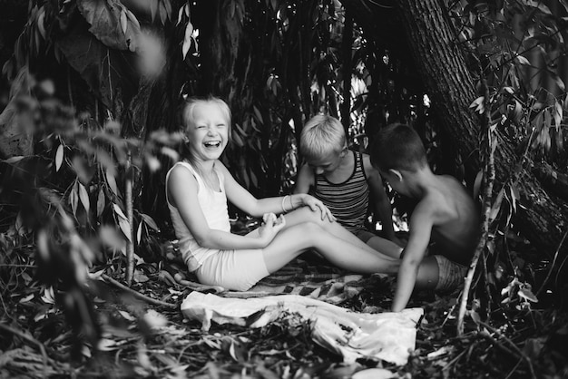 Drie dorpskinderen spelen in een hut die ze zelf hebben gebouwd van bladeren en takjes Houten huis in het bos Zwart-wit fotografie