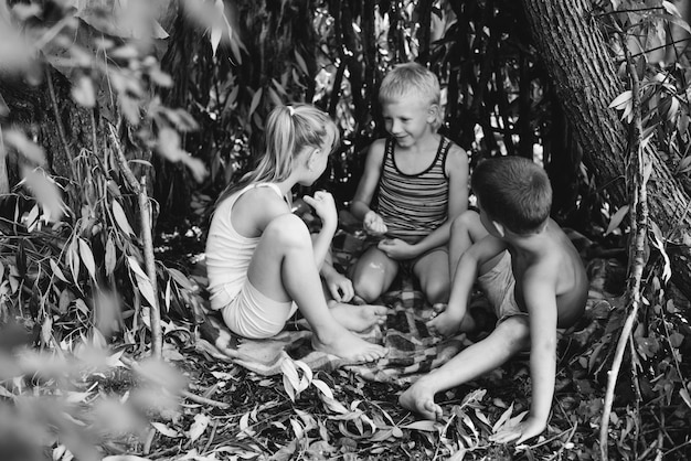 Drie dorpskinderen spelen in een hut die ze zelf hebben gebouwd van bladeren en takjes Houten huis in het bos Zwart-wit fotografie