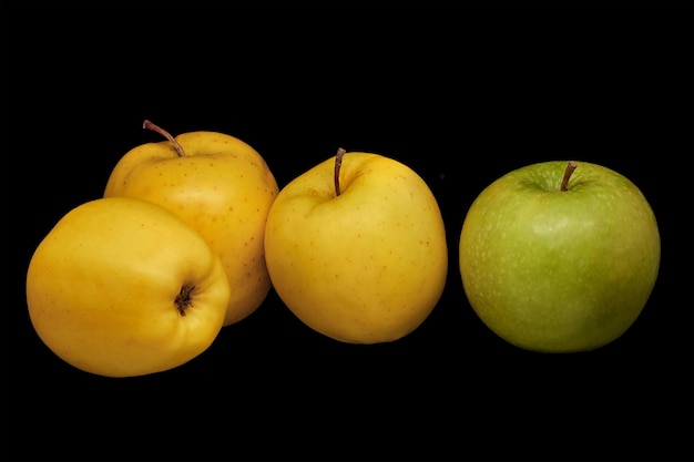 Drie gele appels en een groene op een zwarte achtergrondxA