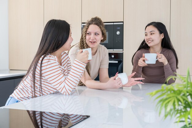 drie gelukkige jonge diversiteitsvriendinnen die thee drinken terwijl ze samen plezier hebben in de moderne keuken