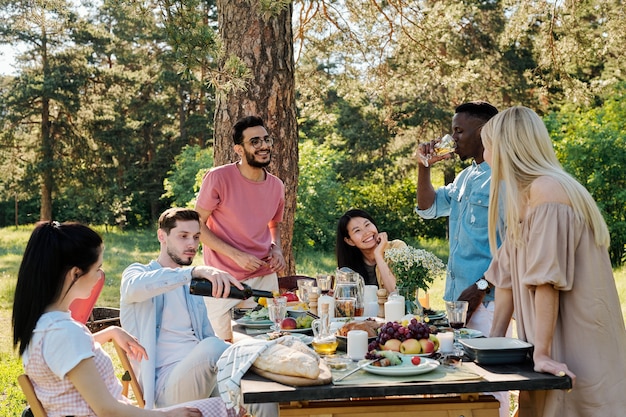 Drie gelukkige jonge interculturele stellen bespreken wat ze gaan doen na het diner buiten terwijl ze aan een gediende tafel zitten