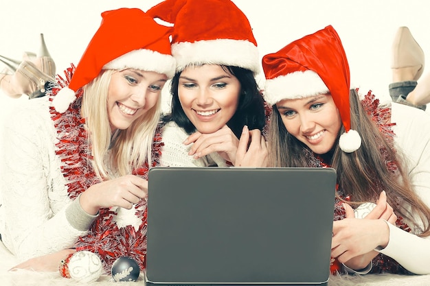 Drie gelukkige jonge vrouwen in kostuums van de kerstman die naar het scherm van de laptop kijken