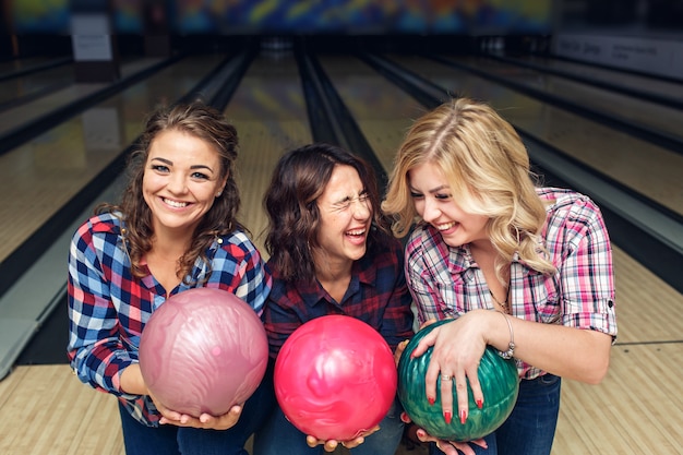 Drie gelukkige meisjes poseren met bowlingballen in club.