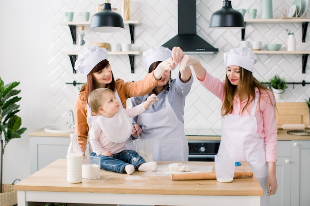 Drie generaties vrouwen in witte schorten maken tot moederdag pizzadeeg in de keuken