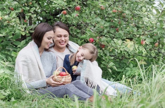 Drie generaties vrouwen van dezelfde familie in een appelboomgaard tijdens een picknick