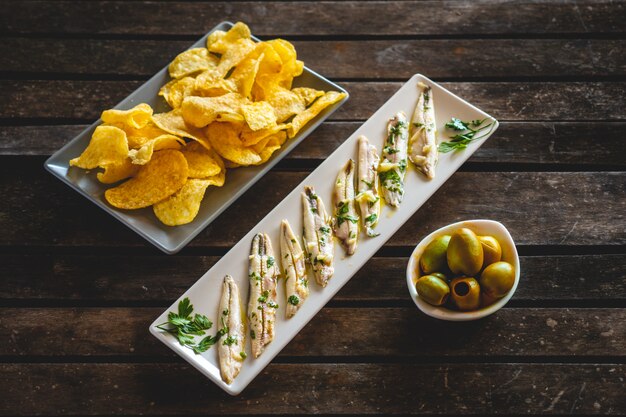 Drie gerechten met chips, geplukte ansjovis en groene olijven op een donkere houten tafel met tandenstokers. Typische Spaanse snacks.