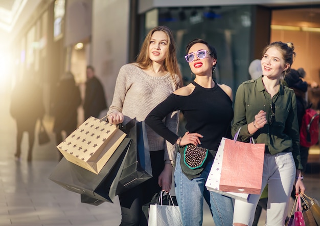 Drie glamoureuze vriendinnen met winkelen papieren zakken lopen