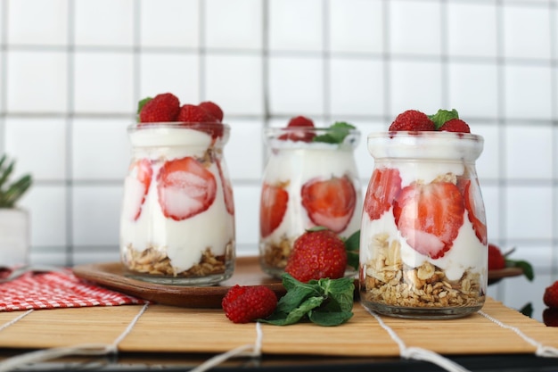 Drie glazen aardbeien parfait gemaakt met verse fruit yoghurt en granola op een houten tafel