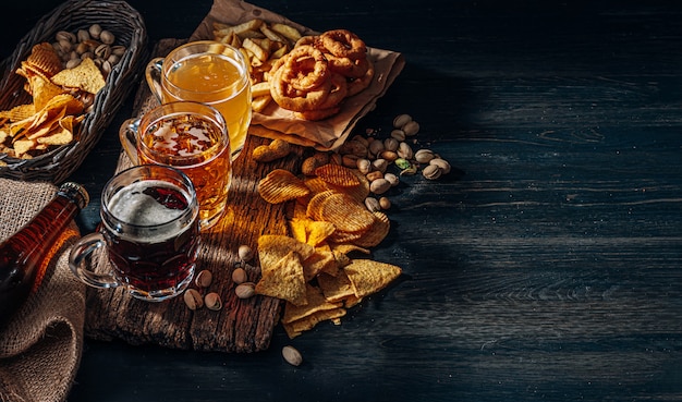 Drie glazen duur ambachtelijk bier, klassiek en ongefilterd en donker in een glas op tafel met een snack van pinda en pistache chips en nacho's